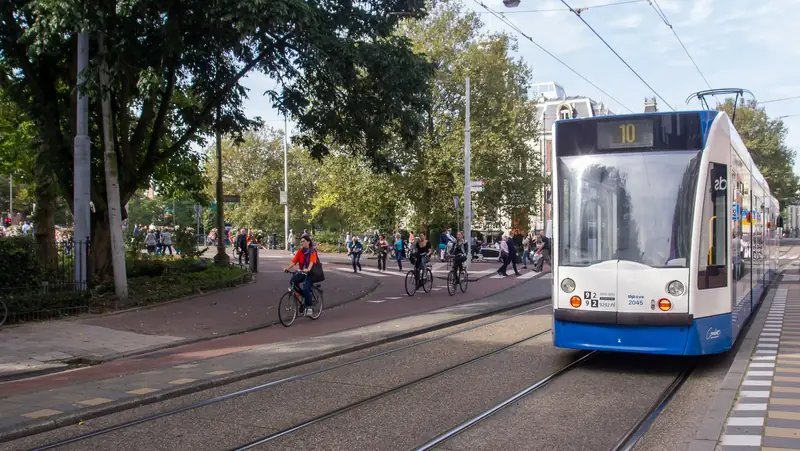 A blue and white tram on line 10 next to a red bike path on Weteringschans in Amsterdam, with several cyclists riding past