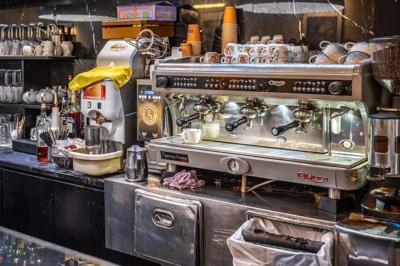 Counter of a coffee bar in Rome with a three-group espresso machine, cups stacked on top to warm and a coffee grinder
