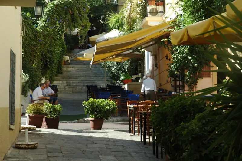 Outdoor taverna tables under yellow awnings on a stepped side street in the Plaka district of Athens